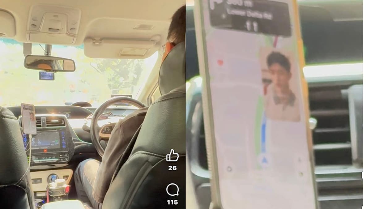 A smartphone mounted on a car dashboard cradle showing a video playing, photographed from the back seat of a moving vehicle in an urban Singapore streetscape.