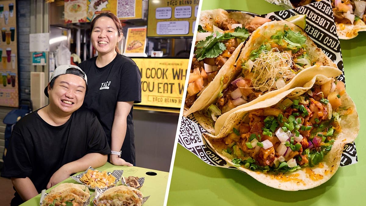A overhead flat-lay of a rustic wooden tray holding a street-food taco with colourful fillings beside a handwritten chalkboard price list, set against a worn hawker centre table surface